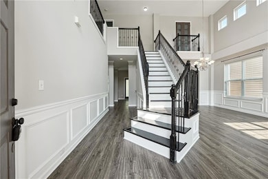 Foyer with stairway, healthy amount of natural light, wood finished floors, a high ceiling, and wainscoting