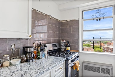 Kitchen with stainless steel range with gas stovetop, tasteful backsplash, radiator heating unit, white cabinets, and light stone countertops