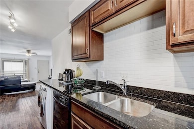 Kitchen featuring dishwasher, washer / dryer, tasteful backsplash, dark stone countertops, and dark wood-style flooring