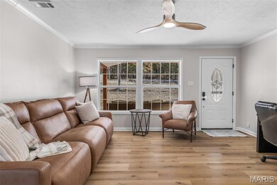 Living room with light wood-style floors, ornamental molding, a textured ceiling, and ceiling fan