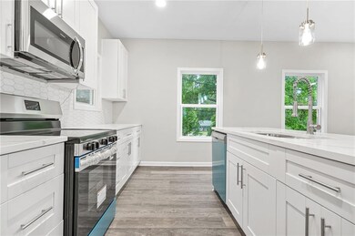 Kitchen with stainless steel appliances, backsplash, white cabinets, light wood-style floors, and decorative light fixtures