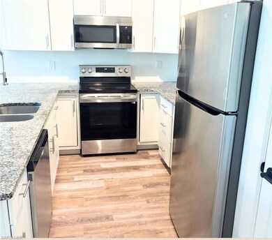 Kitchen with appliances with stainless steel finishes, a sink, light wood-style flooring, and white cabinets