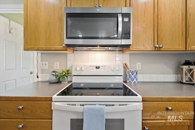 Kitchen featuring white range with electric stovetop, stainless steel microwave, decorative backsplash, brown cabinetry, and dark countertops