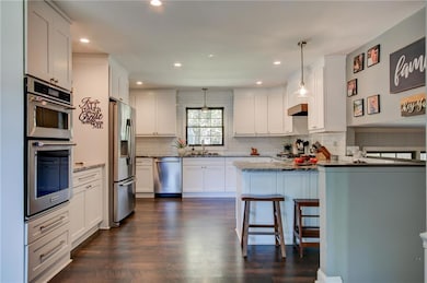 Kitchen featuring light stone countertops, white cabinetry, appliances with stainless steel finishes, a kitchen bar, and dark wood-type flooring
