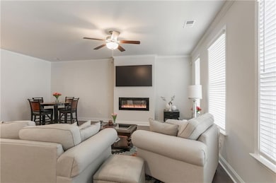 Living room with ceiling fan, a glass covered fireplace, crown molding, and baseboards