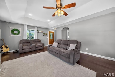 Living area with dark wood-style flooring, a raised ceiling, recessed lighting, a ceiling fan, and arched walkways
