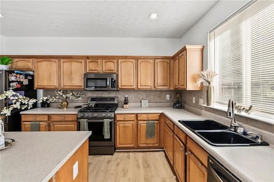 Kitchen with appliances with stainless steel finishes, light wood-type flooring, brown cabinets, a textured ceiling, and recessed lighting
