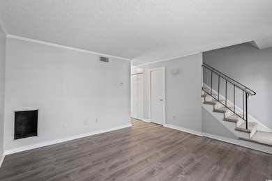 Unfurnished living room featuring wood finished floors, a textured ceiling, stairway, and ornamental molding