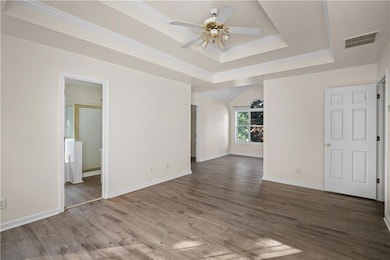 Unfurnished room featuring a tray ceiling, a ceiling fan, wood finished floors, and ornamental molding