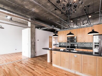 Kitchen with stainless steel appliances, light brown cabinetry, dark countertops, and light wood-style flooring