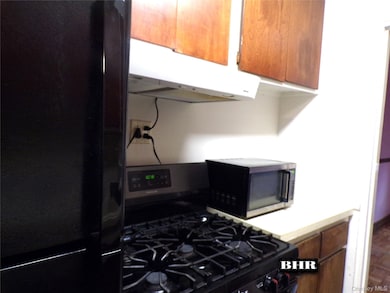 Kitchen featuring range with gas cooktop, freestanding refrigerator, light countertops, under cabinet range hood, and stainless steel microwave