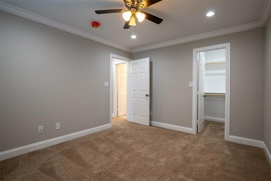 Unfurnished bedroom featuring light carpet, a walk in closet, crown molding, and ceiling fan