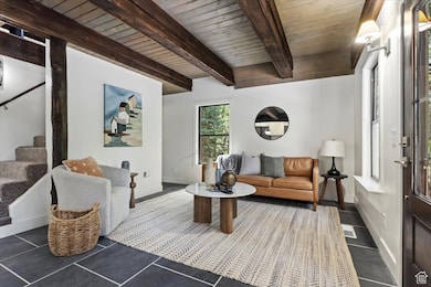 Living room featuring stairway, dark tile patterned flooring, and a wooden ceiling with exposed beams