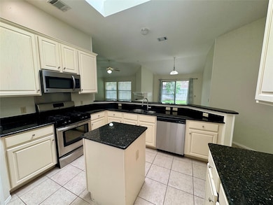 Kitchen with appliances with stainless steel finishes, a skylight, light tile patterned floors, a kitchen island, and vaulted ceiling