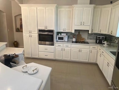 Kitchen with black electric stovetop, tasteful backsplash, stainless steel oven, and light tile floors