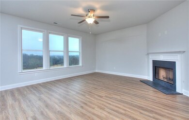 Unfurnished living room with wood finished floors, ceiling fan, and a fireplace with raised hearth