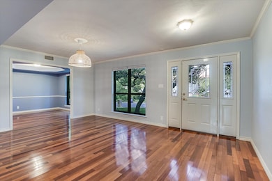 Entrance foyer with crown molding, dark wood-style floors, and arched walkways