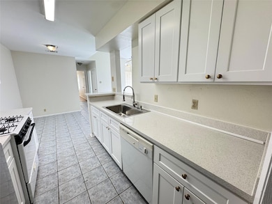 Kitchen with white appliances, light tile patterned floors, white cabinets, and light stone counters