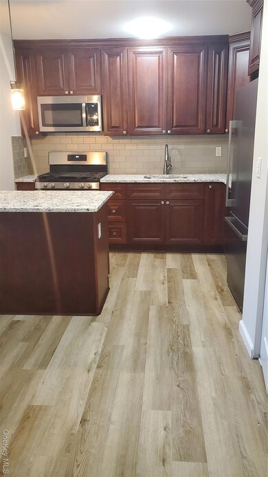 Kitchen featuring decorative backsplash, stainless steel microwave, range, light stone countertops, and refrigerator