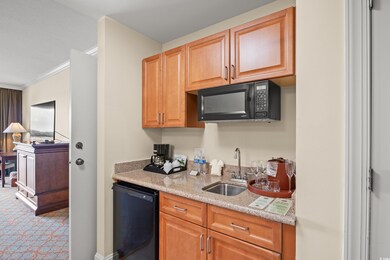 Kitchen featuring black microwave, a sink, refrigerator, light stone counters, and light colored carpet