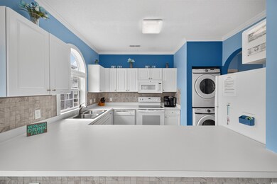 Kitchen featuring white cabinets, white appliances, decorative backsplash, light countertops, and stacked washer / drying machine