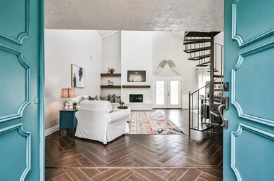 Double front doors open to reveal this light and bright sunken living space with neutral grey paint, soaring ceilings, an eye-catching metal circular staircase, and striking wood-look tile flooring laid in a herringbone pattern.