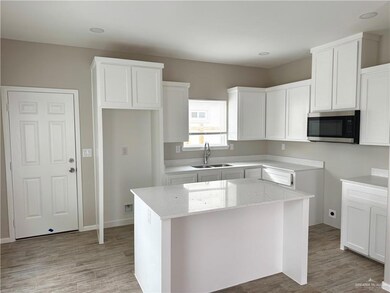 Kitchen featuring stainless steel microwave, a sink, light stone counters, a kitchen island, and white cabinets