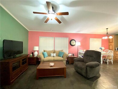 Living room featuring crown molding, ceiling fan with notable chandelier, and dark tile flooring