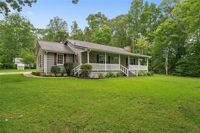 View of front of house featuring a chimney, covered porch, a front yard, and metal roof