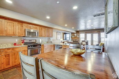 Kitchen featuring stainless steel appliances, light stone countertops, recessed lighting, a peninsula, and brown cabinetry
