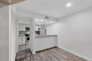 Kitchen featuring decorative backsplash, white cabinets, a textured wall, light wood-style flooring, and a peninsula