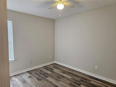 Empty room with dark wood-type flooring, a ceiling fan, a textured ceiling, baseboards, and plenty of natural light