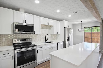 Kitchen featuring stainless steel appliances, light countertops, decorative backsplash, dark wood finished floors, and white cabinets
