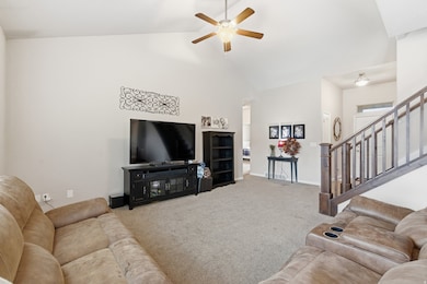 Carpeted living area with high vaulted ceiling, ceiling fan, and stairway