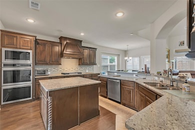 Kitchen with stainless steel appliances, decorative light fixtures, backsplash, custom exhaust hood, and light stone countertops