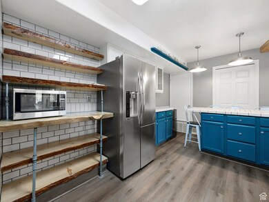 Kitchen with blue cabinets, stainless steel appliances, open shelves, dark wood-type flooring, and decorative light fixtures