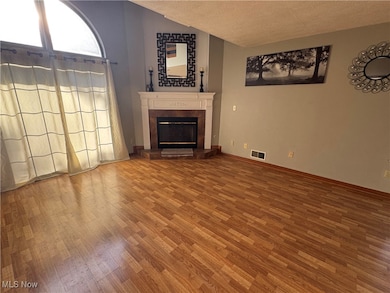Unfurnished living room with a textured ceiling, wood finished floors, a glass covered fireplace, and lofted ceiling