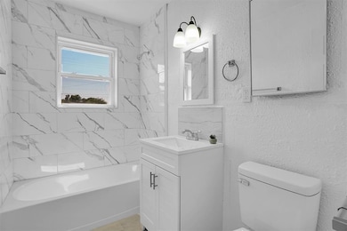 Full bath with a textured wall, vanity, and washtub / shower combination