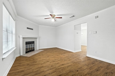 Unfurnished living room with a ceiling fan, a tiled fireplace, a textured ceiling, wood finished floors, and crown molding