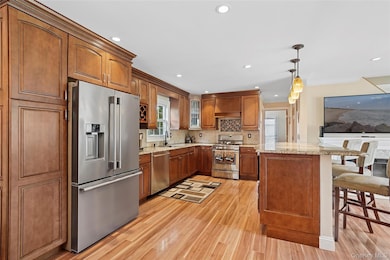 Kitchen with appliances with stainless steel finishes, decorative backsplash, brown cabinetry, light wood finished floors, and a breakfast bar