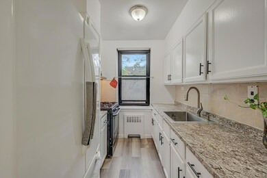 Kitchen with white refrigerator with ice dispenser, backsplash, black gas range oven, radiator, and light wood-type flooring