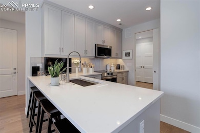 Kitchen featuring appliances with stainless steel finishes, a sink, tasteful backsplash, baseboards, and light wood finished floors