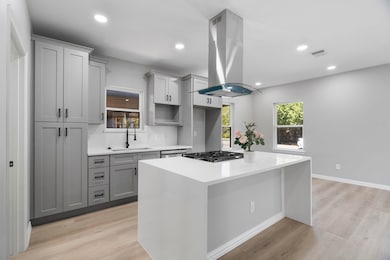 Kitchen with light stone counters, light wood-style floors, island exhaust hood, gray cabinetry, and recessed lighting