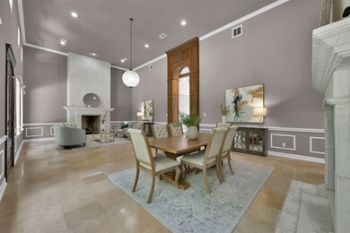 The stunning grand entrance doubles as a dining room and a formal living room. It features dual floor to ceiling fireplaces, travertine marble tile, soaring ceilings, and a gorgeous wood entry to the rest of the home.