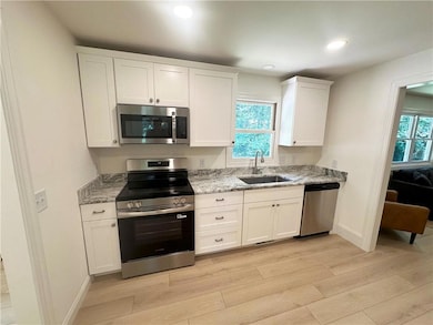 Kitchen with stainless steel appliances, light wood finished floors, light stone counters, white cabinetry, and recessed lighting