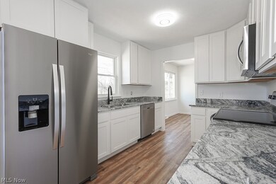 Kitchen with light stone countertops, stainless steel appliances, white cabinetry, sink, and dark hardwood / wood-style flooring