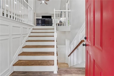 Stairs with a decorative wall, wood finished floors, a ceiling fan, and a wainscoted wall
