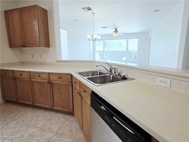 Kitchen with brown cabinetry, light countertops, stainless steel dishwasher, light tile patterned flooring, and a chandelier