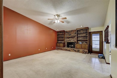 Unfurnished living room featuring a textured ceiling, a ceiling fan, built in features, carpet flooring, and a fireplace