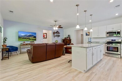 Kitchen featuring appliances with stainless steel finishes, open floor plan, light wood-style floors, white cabinetry, and a kitchen island